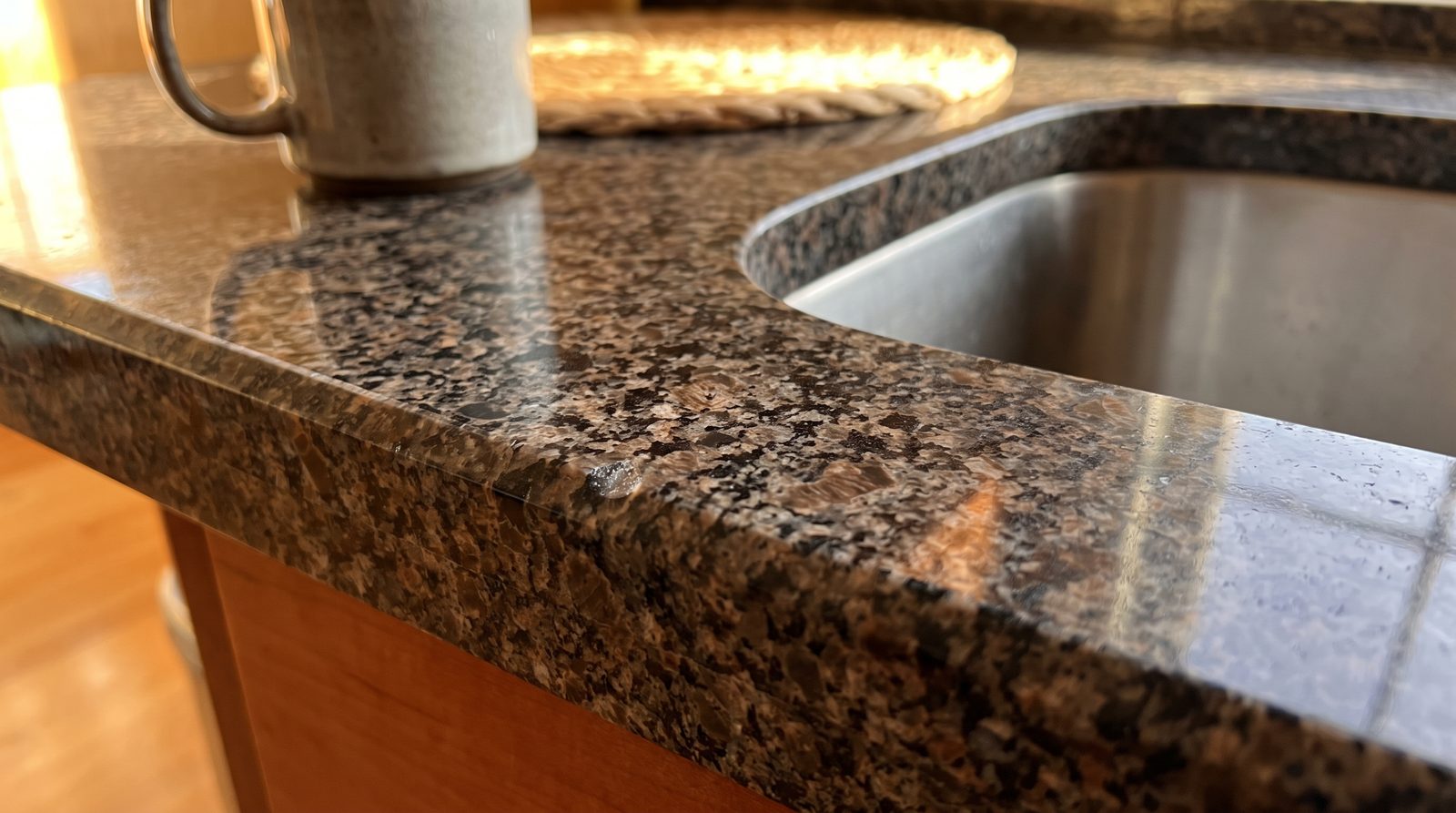 Repaired chip on a dark granite countertop edge polished flush beside a sink