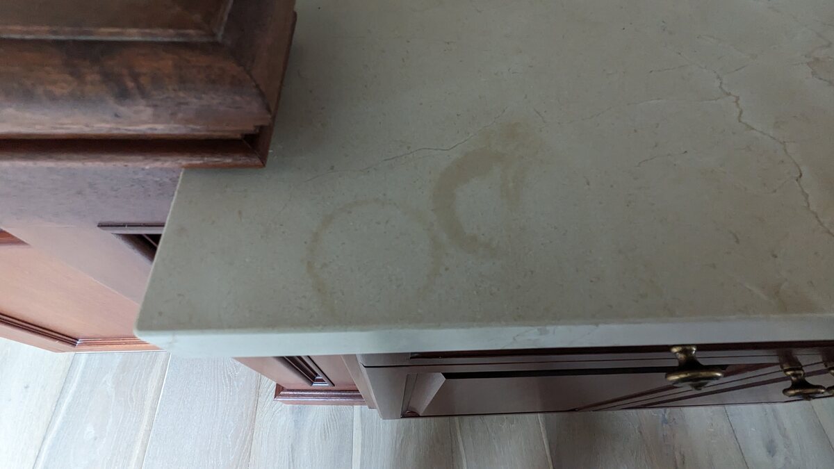 Ring marks and staining left on a pale stone kitchen countertop